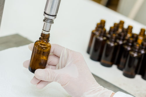 Close up of female lab worker hand with gloves filling the bottle with liquid..